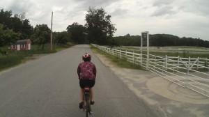 Deb cycling beside horse corral